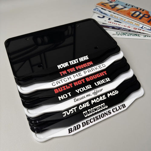NG Frames custom acrylic license plate frames in black and white with various witty slogans stacked on a table.